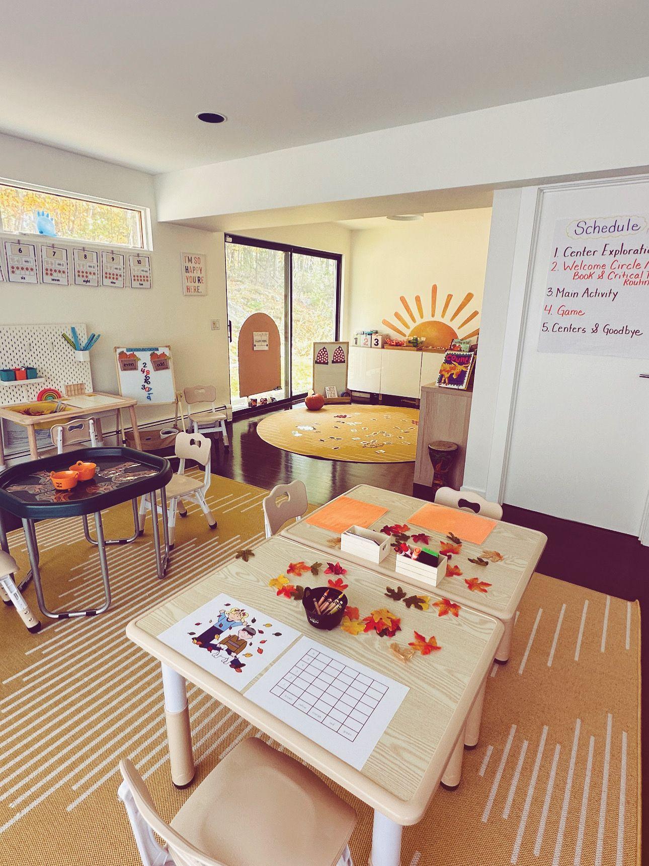 Bright classroom with children's tables, chairs, craft supplies, and educational posters on the walls.