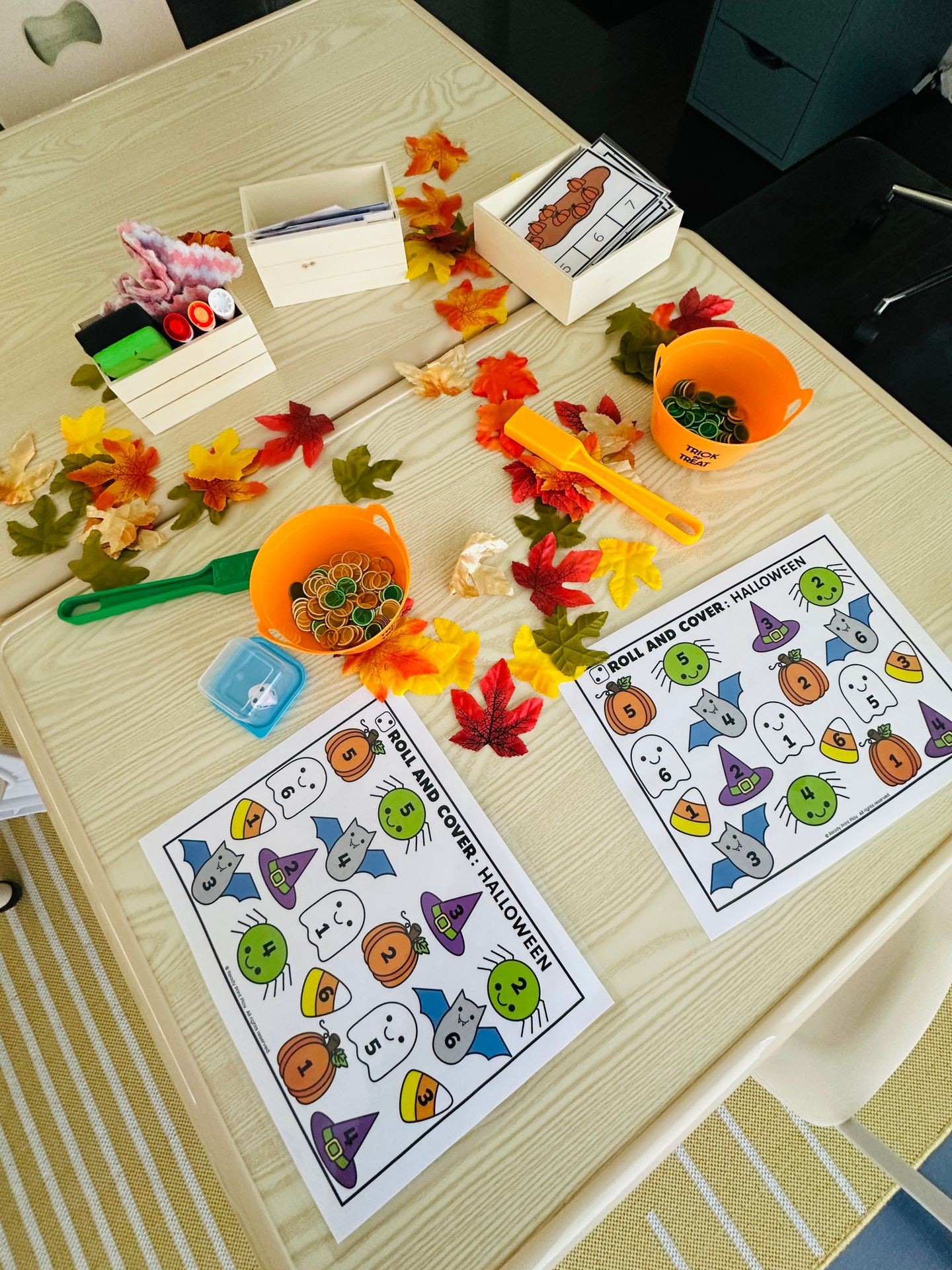 Halloween-themed activity setup with worksheets, orange buckets, and autumn leaves on a table.