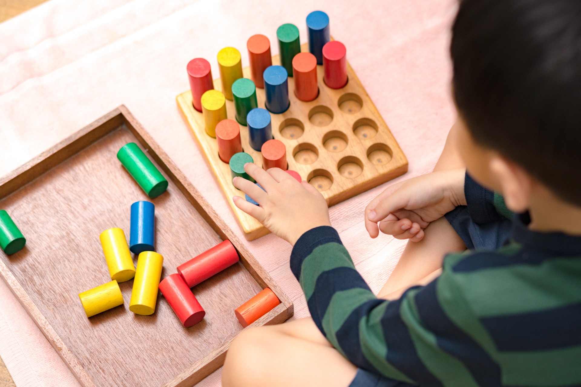 Cute Asian Montessori preschool boy student sitting, learning and playing with colorful wooden cylinder socket.